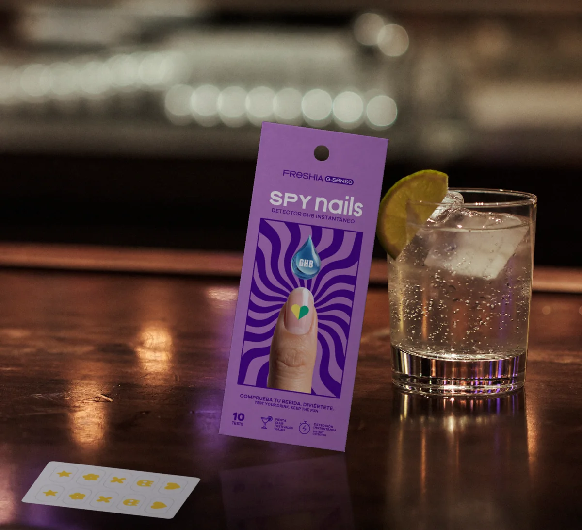 Spy Nails apoyado en una copa en la barra de un bar, con la lámina de pegatinas delante.